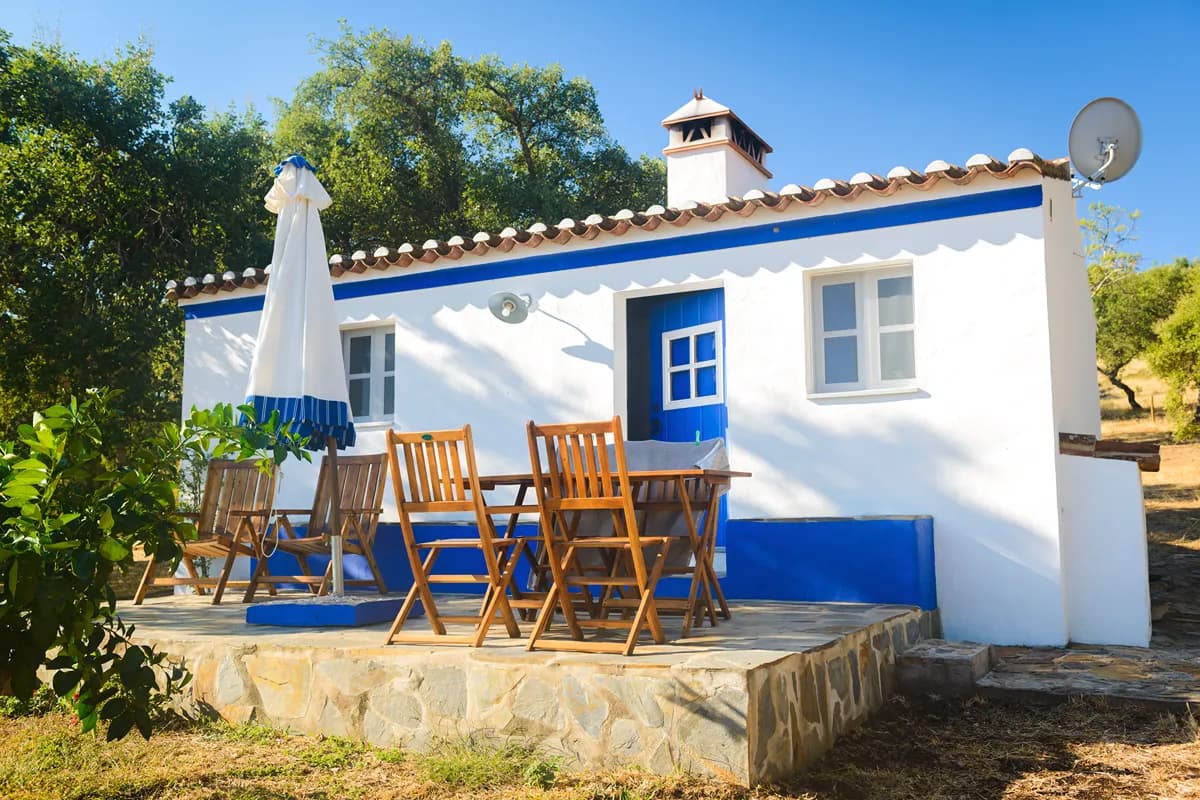 Whitewashed Alentejo country house with a shaded outdoor terrace, trees, and dining area