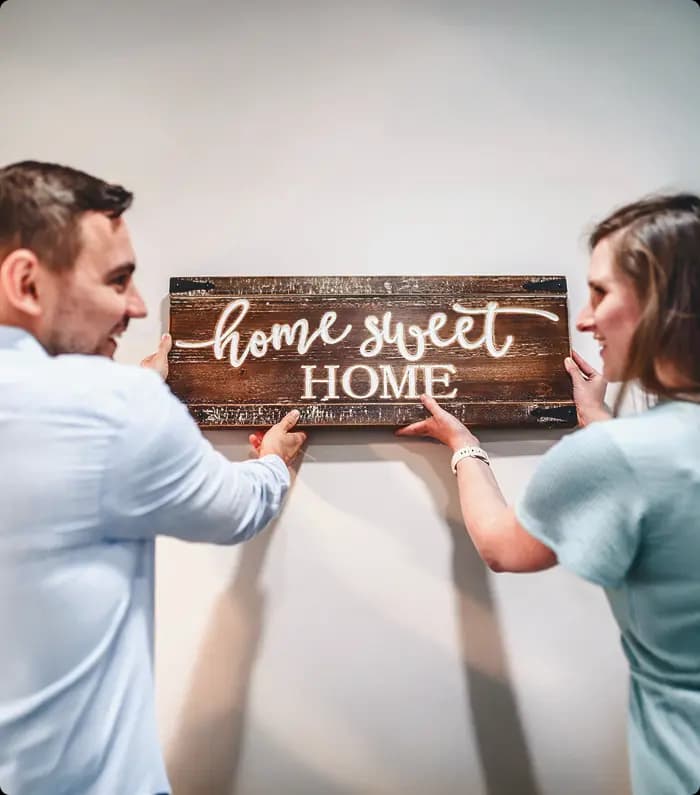Smiling couple placing a wooden "home sweet home" plate in their new house