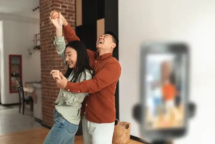 Couple dancing and laughing at home while a smartphone records on a tripod