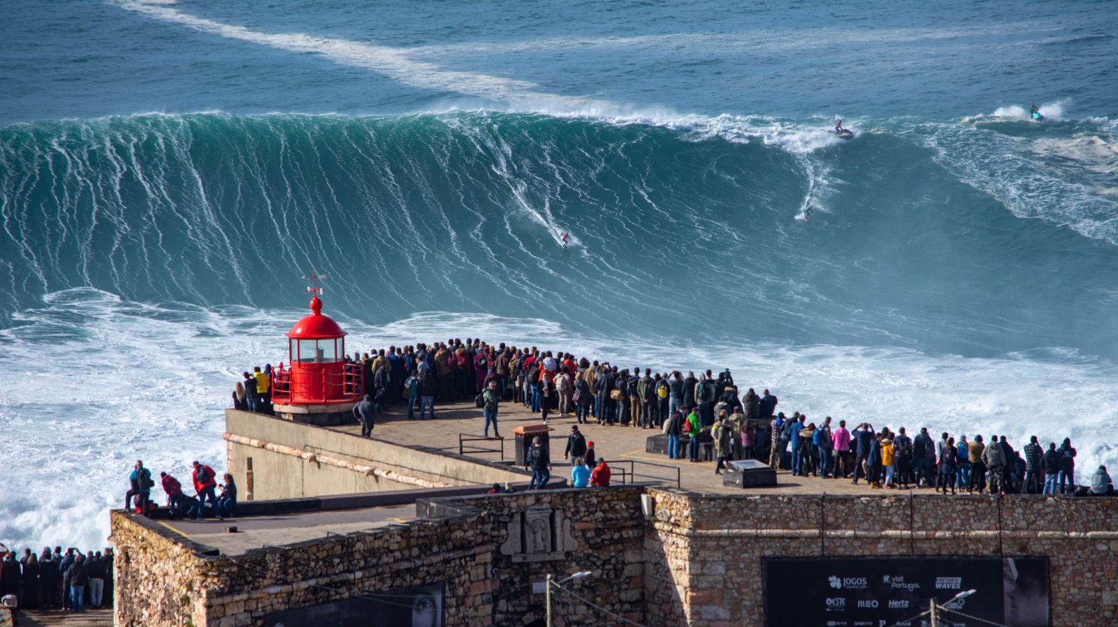 Crowd observing huge waves and surfers in Nazaré.